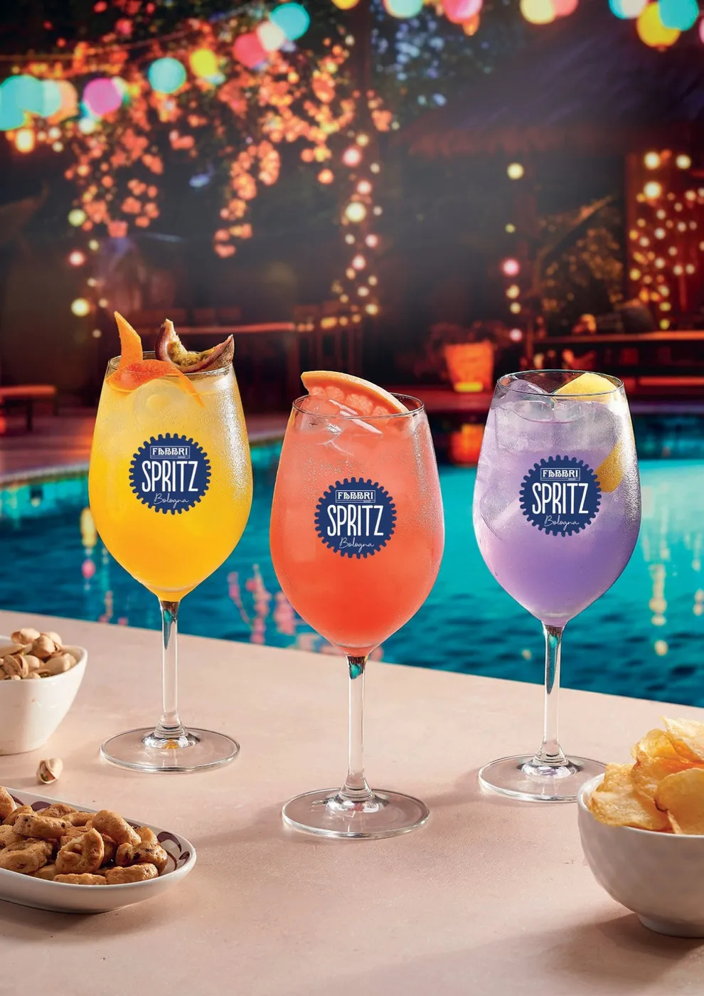 Tre gota Fabbri Spritz në ngjyra portokalli, rozë dhe vjollcë pranë pishinës